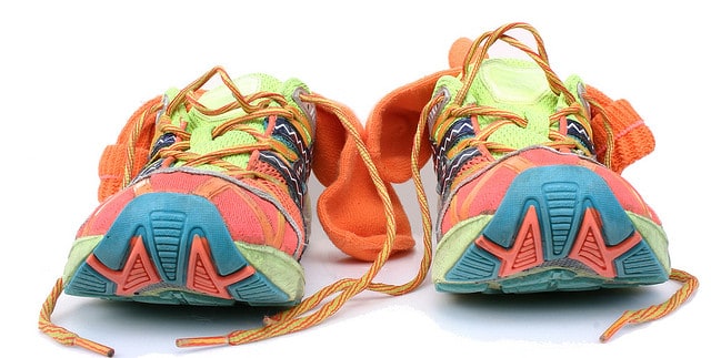 A pair of colorful running shoes facing forward. The shoes feature vibrant hues of green, orange, blue, and pink, with multicolored laces and soles. An orange pair of socks is placed between the shoes.