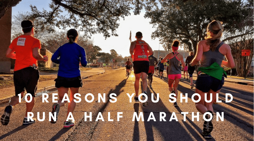 A group of runners in athletic gear are jogging on a sunny street framed by trees. The text on the image reads "10 Reasons You Should Run a Half Marathon." Sunlight casts long shadows as the runners proceed down the road, some wearing race numbers.