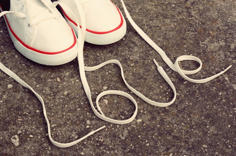 A pair of white canvas sneakers with red trim are placed on a textured concrete surface. The shoelaces are arranged to form the word "LOVE" on the ground in front of the shoes.