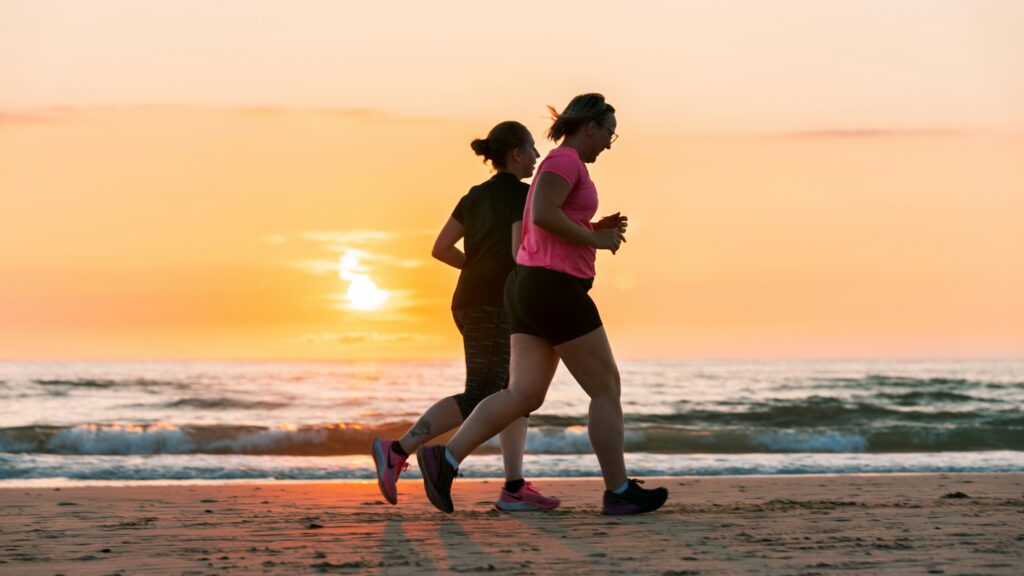 Two women jogging on the bay of a beach with a beautiful sunset background.