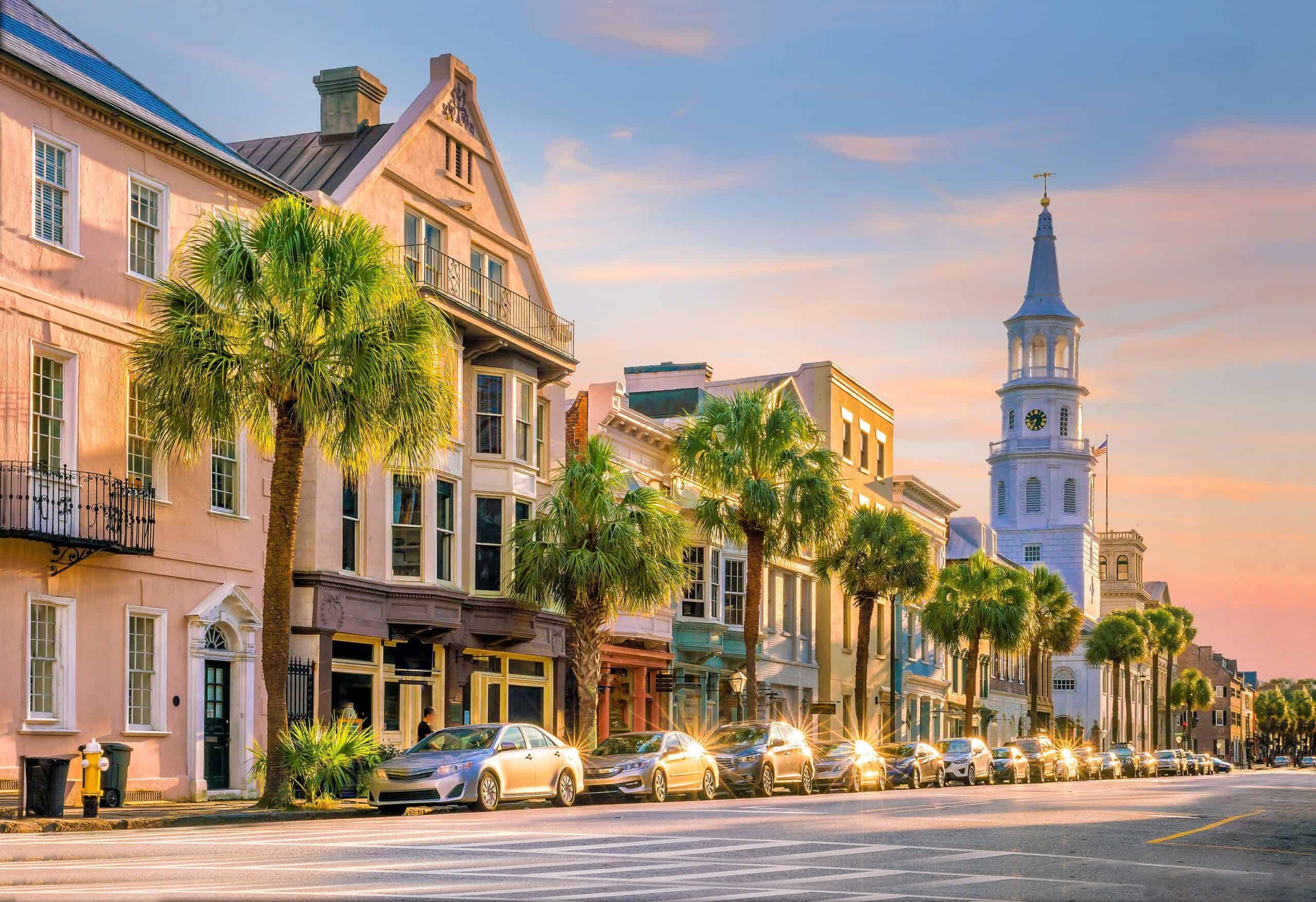 A picturesque street lined with colorful, historic buildings and palm trees features prominently in one of the best half marathon routes in the southeast. The street is filled with parked cars, and a tall church steeple is visible in the background against a vibrant evening sky.