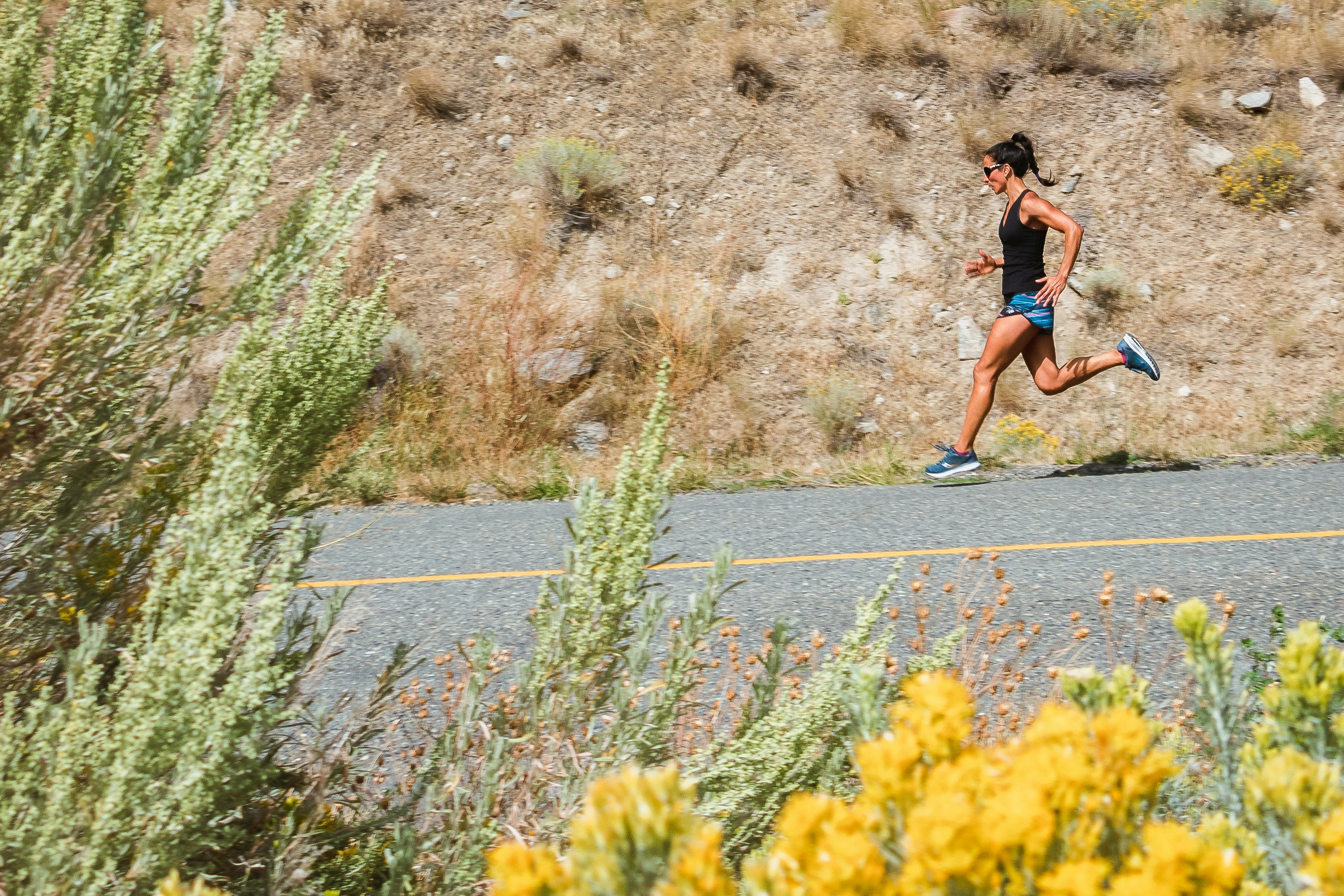 Woman with sunglasses running downhill in a desert environment.