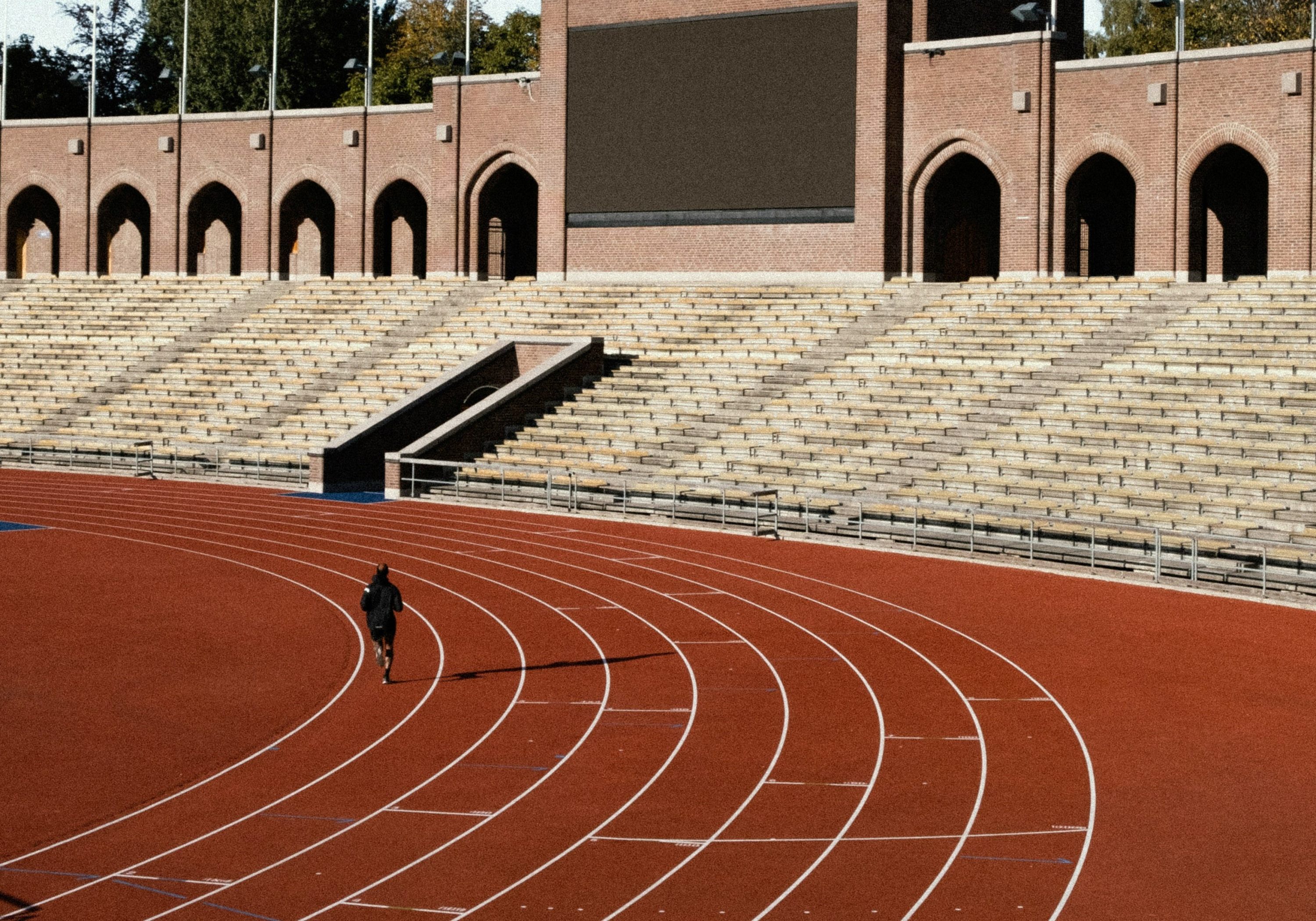 A person doing track workouts for runners at a high school with a stadium in the background.