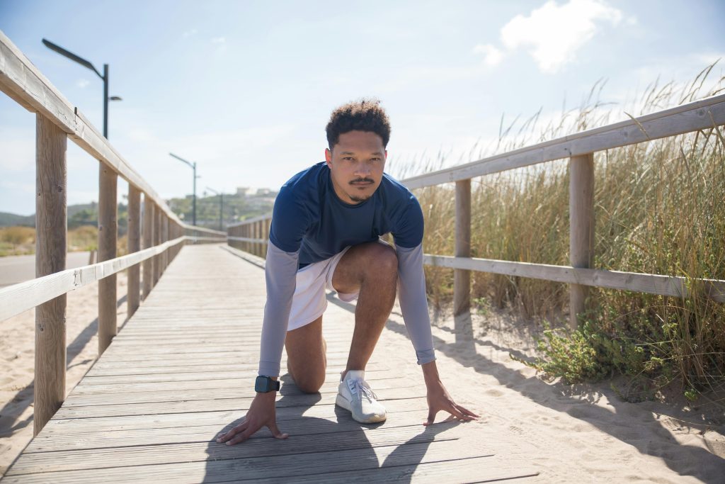 A male runner training for a marathon, getting ready to take off on a boardwalk at the beach